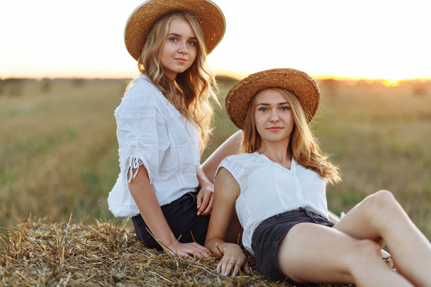 Portrét dvou dívek v slaměné klobouky na kupce sena - Fotografie, Obrázek