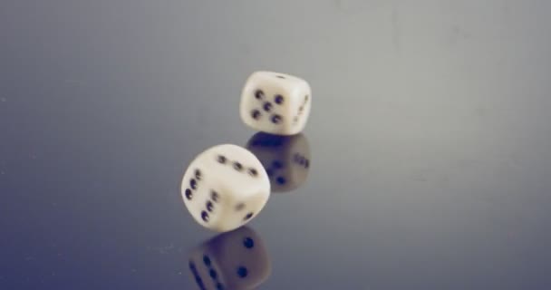 Slow motion macro shot of white dice falling and rolling on reflective surface - Video