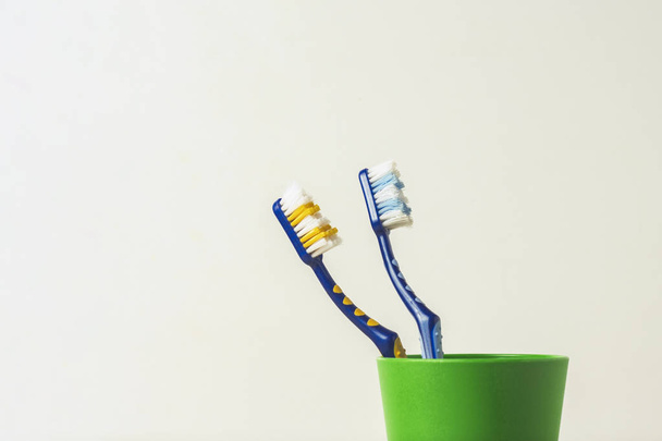 Two used toothbrushes in a plastic cup on a white background. The concept of changing toothbrushes, oral hygiene, dentistry, friendly family. - Photo, Image