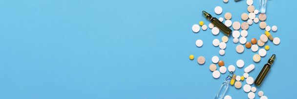 Pilules de différentes couleurs et ampoules avec médicament sur un fond bleu. Concept de l'industrie pharmaceutique, la médecine, le traitement et la récupération après la maladie. Bannière. Couché plat, vue du dessus
 - Photo, image