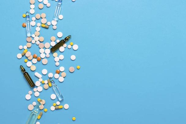Таблетки разных цветов и ампулы с лекарствами на синем фоне. Концепция фармацевтической промышленности, медицины, лечения и восстановления после болезни. Плоский, вид сверху
 - Фото, изображение