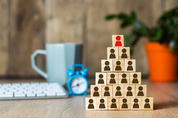 Wooden cubes with men lined up with a pyramid on the background of the office desk. Concept of corporation, financial pyramid, leadership. - Foto, afbeelding