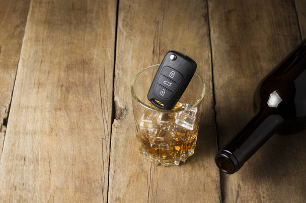 Autoschlüssel in einem Glas mit einem alkoholischen Getränk und einer leeren Flasche auf einem hölzernen Hintergrund. Trunkenheit am Steuer, Alkohol am Steuer. - Foto, Bild