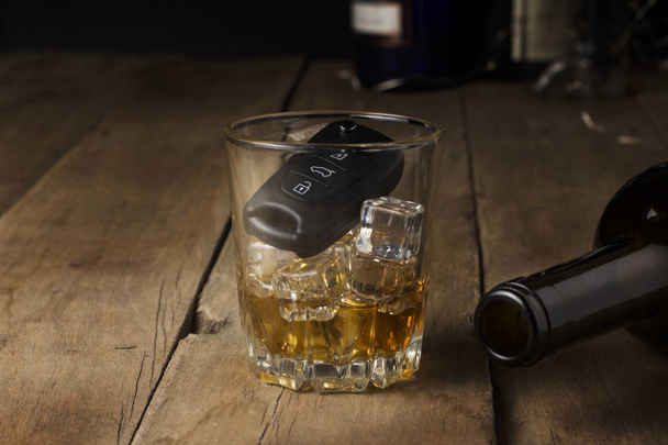 Autosleutels in een glas met een alcoholische drank en een lege fles op een houten achtergrond. Dronken rijden concept, stop drinken en rijden. - Foto, afbeelding