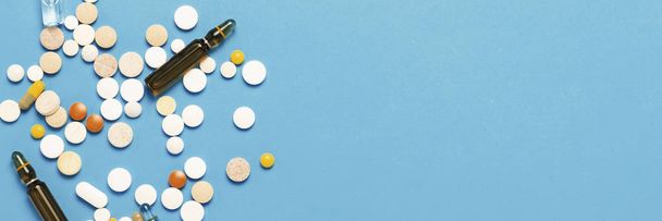 Pills of different colors and ampoules with medicine on a blue background. Concept of the pharmaceutical industry, medicine, treatment and recovery after illness. Banner. Flat lay, top view - Photo, Image