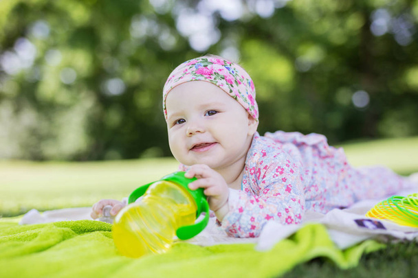 Vrolijk babymeisje met fles water in de zomer park - Foto, afbeelding