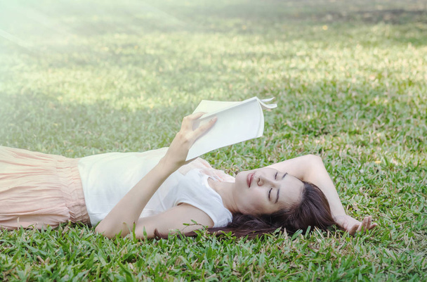 Woman lying on grass field for reading in the park - Photo, Image