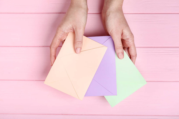Female hands with colorful paper envelopes on pink wooden table - Foto, imagen