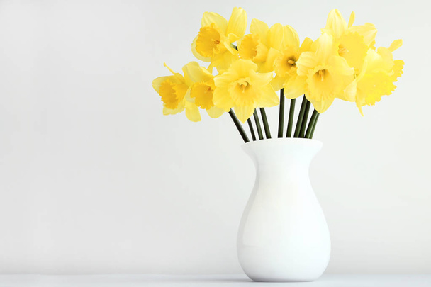Yellow narcissus flowers in vase on grey background - Photo, image