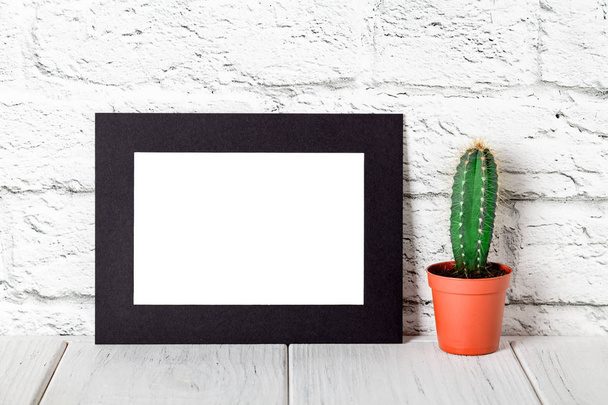 Черный картон фото рамка на белом столе против кирпичной стены. Образец кирпичной стены. Mockup
 - Фото, изображение