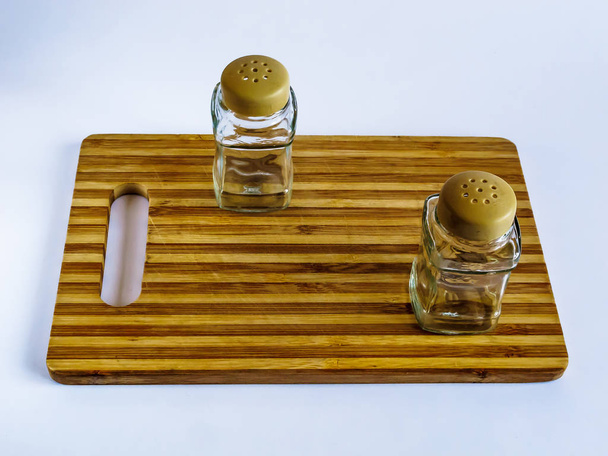 Pimienta olla y salero pie vacío en una tabla de cortar sobre un fondo blanco
 - Foto, imagen