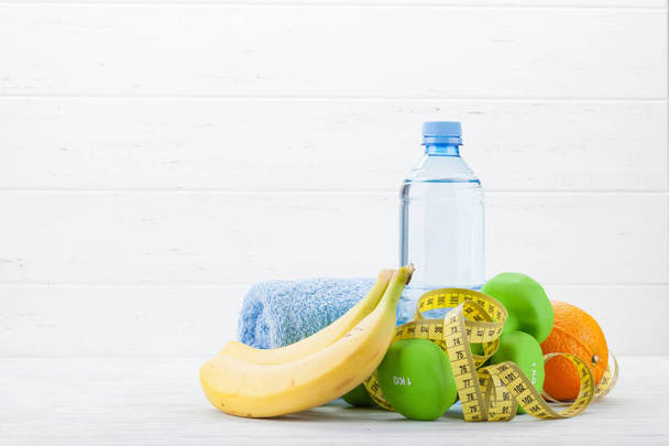 Činky, ovoce, láhev a ručník na dřevěný stůl - Fotografie, Obrázek