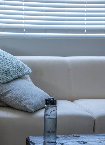 eine Glasflasche Wasser auf einem Beistelltisch in einer kühlen Ecke eines modernen Lounge-Bildes mit Kopierraum im Hochformat - Foto, Bild