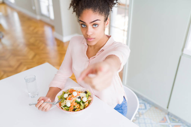 Молодая африканская американка ест здоровый салат из макарон, указывая пальцем на камеру и на вас, знак руки, позитивный и уверенный жест спереди
 - Фото, изображение
