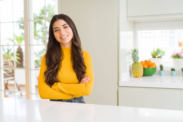Young beautiful woman at home on white table happy face smiling with crossed arms looking at the camera. Positive person. - Photo, Image