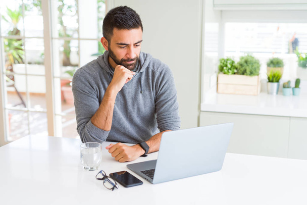 Hombre hispano guapo trabajando con computadora portátil cara seria pensando en la pregunta, idea muy confusa
 - Foto, imagen