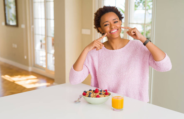 Mladá africká americká žena s zdravou snídani ráno doma s úsměvem sebevědomá ukazující a ukazující prsty zuby a ústa. Koncepce zdraví. - Fotografie, Obrázek