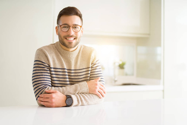 Όμορφος νεαρός που φοράει γυαλιά στο σπίτι με ένα χαρούμενο πρόσωπο στέκονται και να χαμογελούν με αυτοπεποίθηση χαμόγελο δείχνει τα δόντια - Φωτογραφία, εικόνα