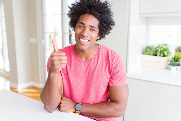 Homem de negócios afro-americano vestindo camiseta casual rosa fazendo polegares felizes gesto com a mão. Aprovando expressão olhando para a câmera mostrando sucesso
. - Foto, Imagem