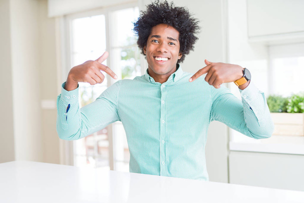 Hombre de negocios afroamericano con camisa elegante que mira confiado con sonrisa en la cara, señalándose con los dedos orgullosos y felices
. - Foto, imagen