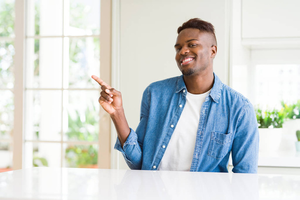 Handsome african american man at home with a big smile on face, pointing with hand and finger to the side looking at the camera. - Foto, imagen