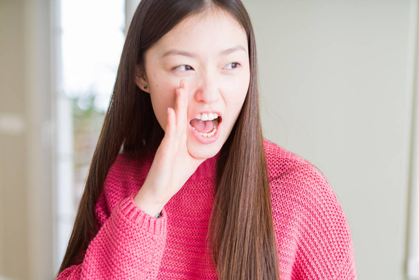 Красиві азіатські жінки носять рожевий светр кричати і кричали гучним на свій бік руки на рот. Спілкування концепції. - Фото, зображення
