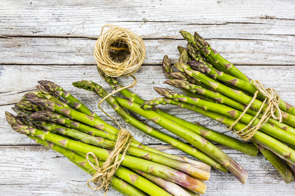 Fresh and raw green asparagus bunches on a wooden background.  - Foto, afbeelding