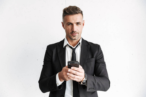 Handsome business man posing isolated over white wall background using mobile phone. - Φωτογραφία, εικόνα