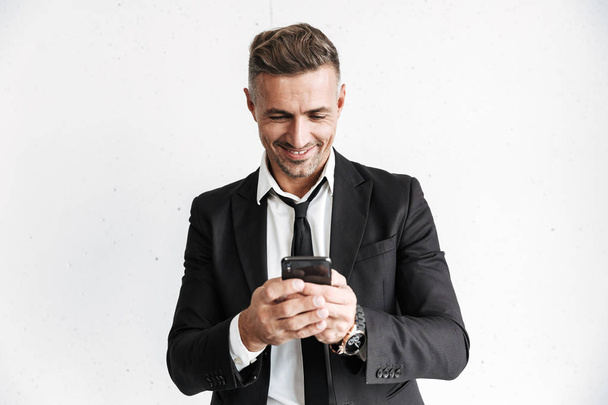 Happy business man posing isolated over white wall background using mobile phone. - Foto, imagen