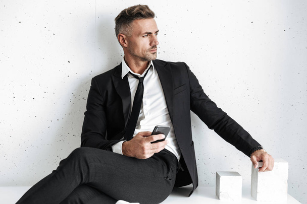 Business man posing isolated over white wall background using mobile phone. - Valokuva, kuva