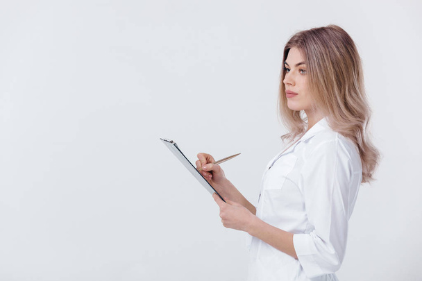 Medische arts arts vrouw in witte jas houdt map met documenten op een lichte achtergrond. - Foto, afbeelding