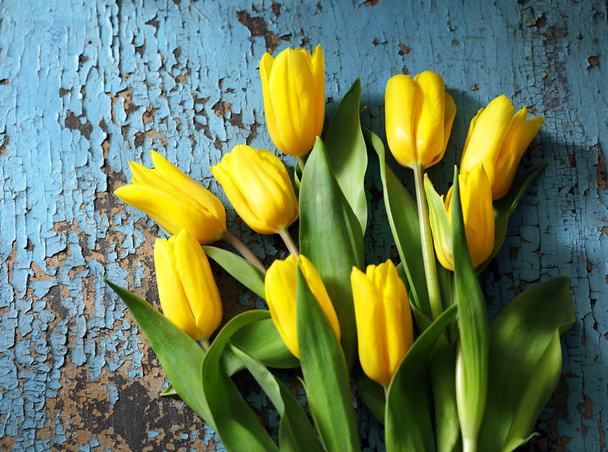 A bouquet of yellow tulips on an old blue wooden table. - Фото, изображение
