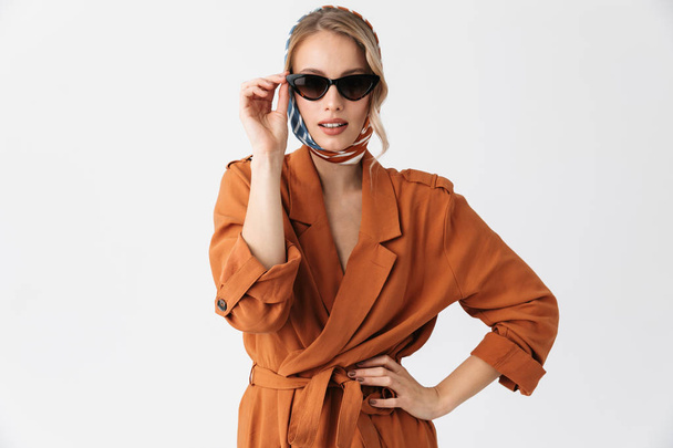 Beautiful young woman wearing silk stylish scarf posing isolated over white wall background wearing sunglasses. - 写真・画像