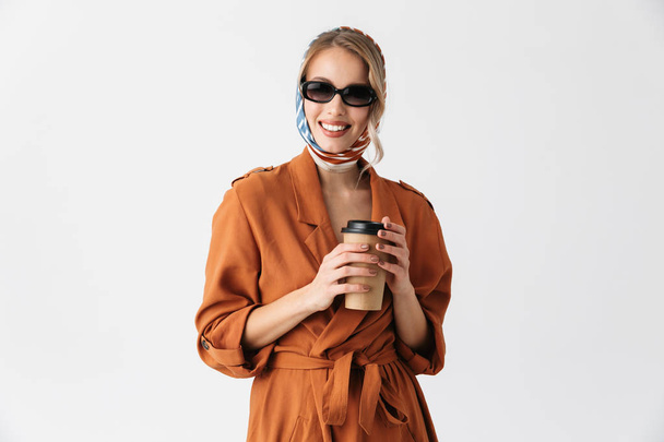 Blonde pretty woman wearing silk scarf and sunglasses posing isolated over white wall background holding cup with coffee. - Foto, Bild