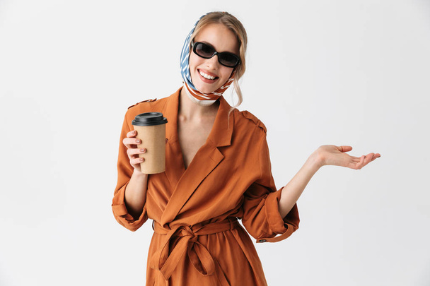 Blonde pretty woman wearing silk scarf and sunglasses posing isolated over white wall background holding cup with coffee. - Foto, Bild