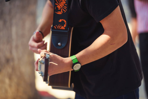 Guy hraje na kytaru na ulici. Pouliční hudebník. Zelený Náramkové hodinky na ruce toho chlapa. Hraní akustické kytary. - Fotografie, Obrázek
