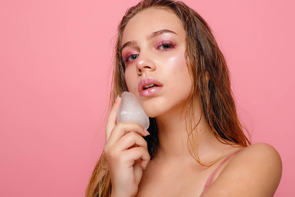 young woman applies the ice to face on a pink background. - Foto, Bild