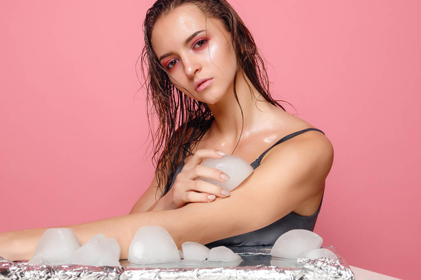young woman applies the ice to face on a pink background. - Foto, imagen