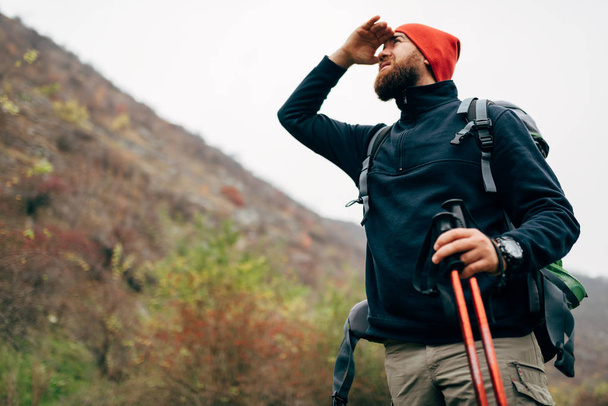 Outdoor horizontal shot of handsome hiker young man hiking in mountains with travel backpack. Traveler bearded male have a break after trekking during vacation, looks away. Travel, people, lifestyle - Fotografie, Obrázek