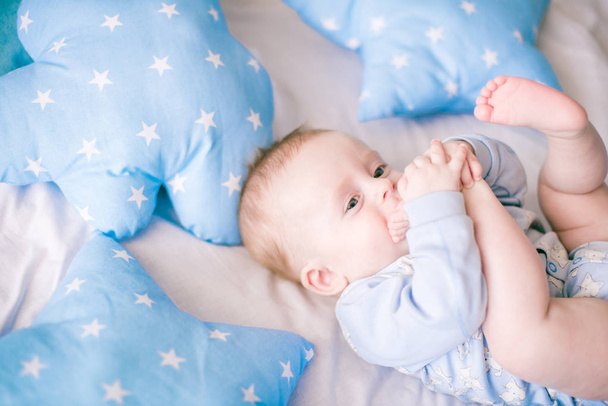 Cute toddler boy on bed at home surrounded by blue pillows - 写真・画像