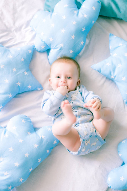 Cute toddler boy on bed at home surrounded by blue pillows - Fotó, kép