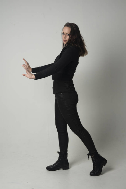 modern siyah ceket ve pantolon giyen bir esmer kız ayakta poz gri studio arka plan üzerinde tam uzunlukta portresi. - Fotoğraf, Görsel