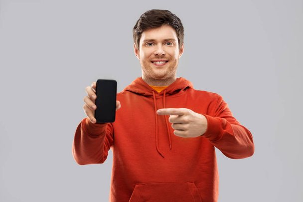 smiling man in red hoodie showing black smartphone - Foto, Imagen