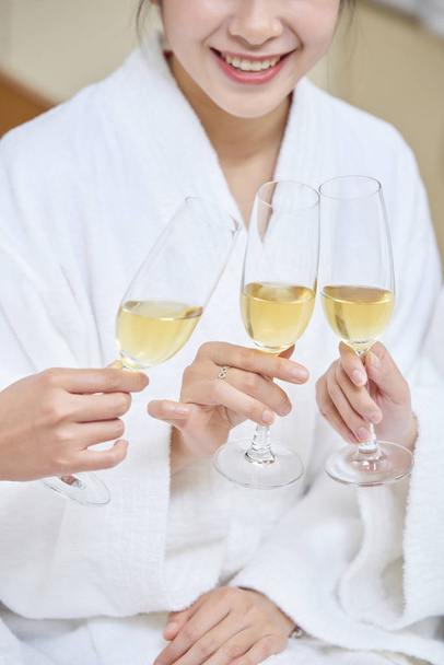 Close-up van lachende jonge vrouw in badjas met champagneglazen samen met haar vrienden in spa salon - Foto, afbeelding