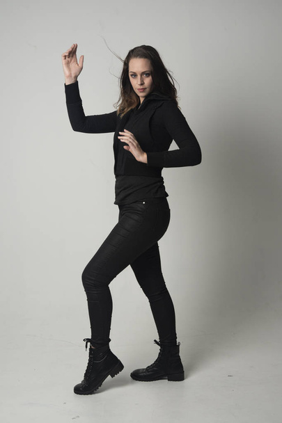 retrato de longitud completa de una chica morena con chaqueta y pantalones negros modernos, de pie posan sobre fondo gris estudio
. - Foto, Imagen