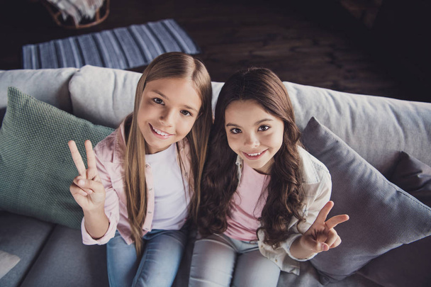 Above high angle view of two nice sweet adorable lovely attractive cheerful cheery girls embracing showing v-sign sitting on divan in house indoors - Zdjęcie, obraz