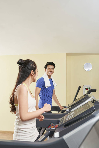 junges asiatisches Paar läuft auf Laufbändern und unterhält sich beim Sport-Training im Fitnessstudio - Foto, Bild