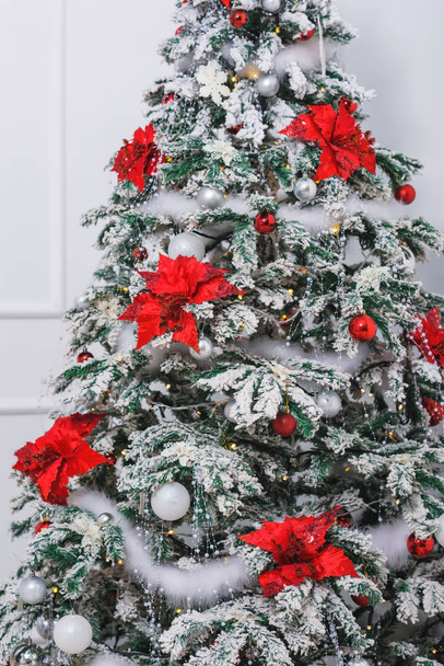 Weihnachtsbaum. rotes und silbernes Spielzeug. Leuchtende Girlanden. Weihnachtsbaum mit Weihnachtssternen geschmückt weißes Lametta aus Federn. - Foto, Bild