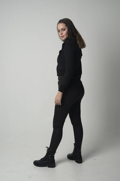 full length portrait of a brunette girl wearing  modern black jacket and pants, standing pose  on grey studio background. - 写真・画像