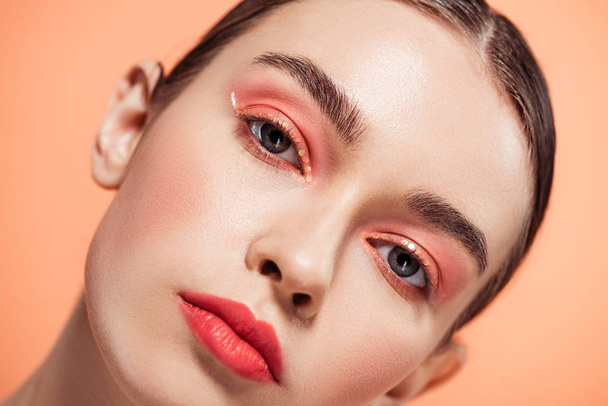 beautiful stylish young woman with glitter makeup looking at camera and posing isolated on coral - Foto, Imagem